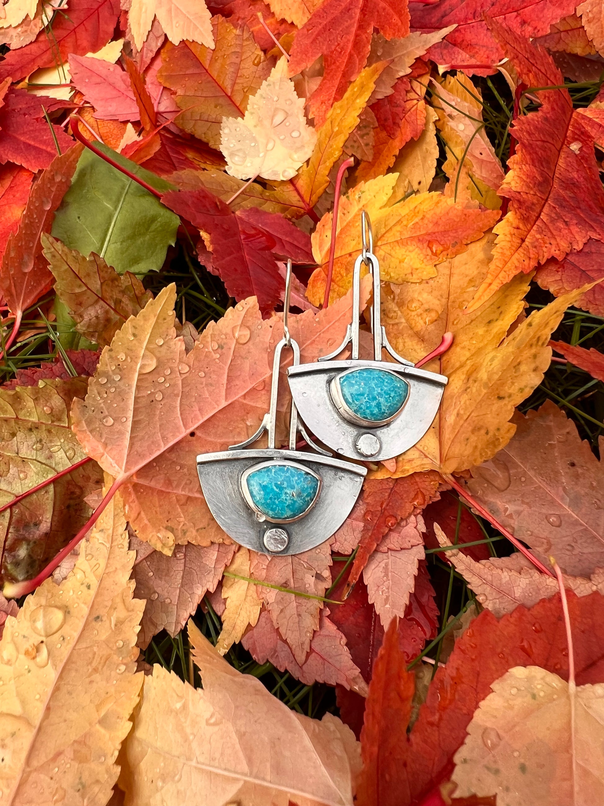 These handcrafted earrings feature Persian Turquoise with delicate white webbing. Framed in sterling silver, art deco in shape with a swooping half circle and elongated lines. They hang from a custom silver ear wire.&nbsp;